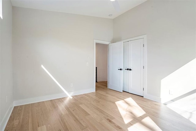 unfurnished bedroom featuring baseboards, light wood-type flooring, a closet, and high vaulted ceiling