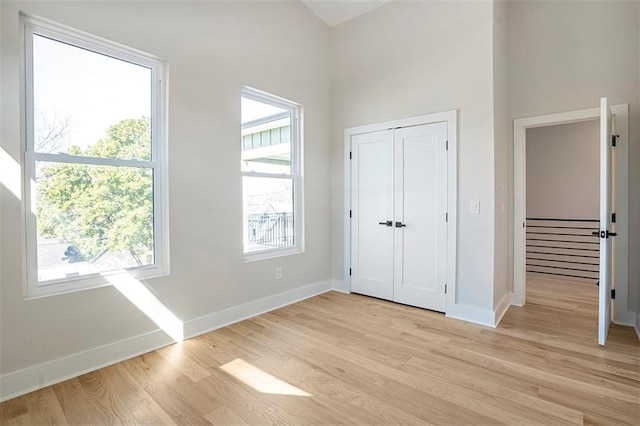 unfurnished bedroom featuring a towering ceiling, baseboards, light wood-type flooring, and a closet