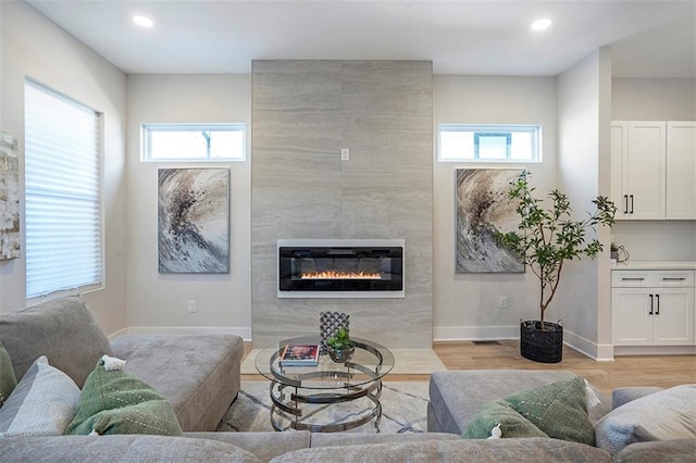 living area featuring baseboards, a healthy amount of sunlight, a high end fireplace, and light wood finished floors