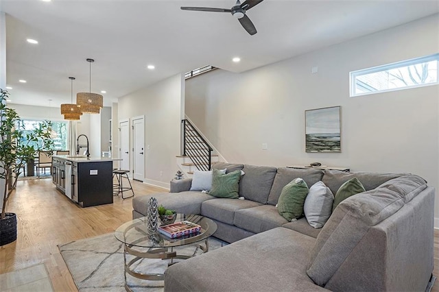 living area with light wood-type flooring, recessed lighting, stairway, baseboards, and ceiling fan