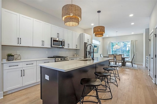 kitchen with a kitchen island with sink, a sink, appliances with stainless steel finishes, white cabinets, and light wood finished floors