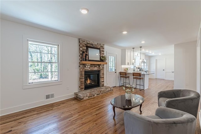 living area with visible vents, a healthy amount of sunlight, a fireplace, and wood finished floors