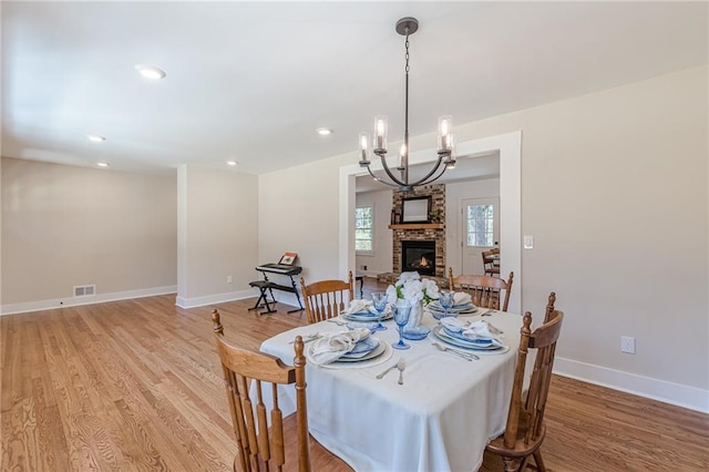 dining area with light wood finished floors, visible vents, baseboards, a chandelier, and a fireplace