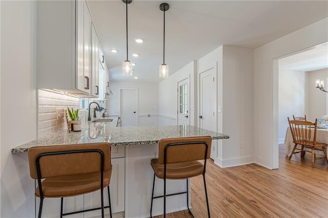 kitchen with backsplash, light stone countertops, light wood-type flooring, a peninsula, and white cabinetry