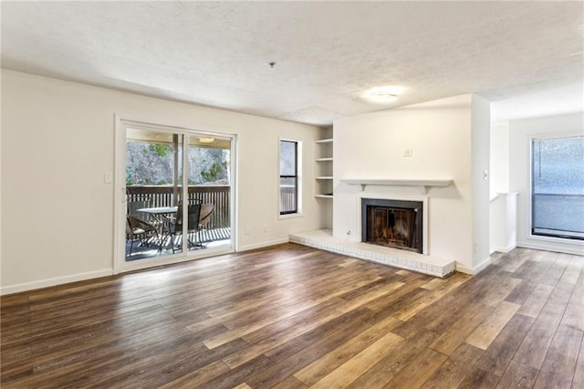 unfurnished living room featuring a textured ceiling, dark wood-type flooring, built in features, baseboards, and a brick fireplace