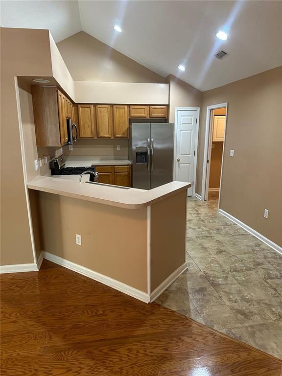 2191 Rockbridge Rd Unit 2603, Stone Mountain, GA 30087 - kitchen featuring stainless steel appliances, brown cabinets, vaulted ceiling, a peninsula, and light countertops