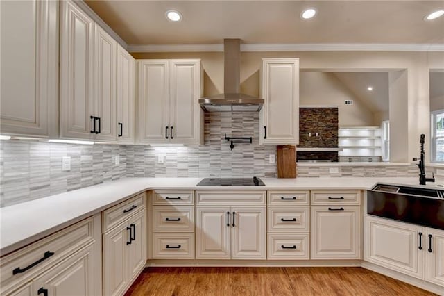 kitchen with wall chimney range hood, black electric stovetop, a sink, light countertops, and backsplash