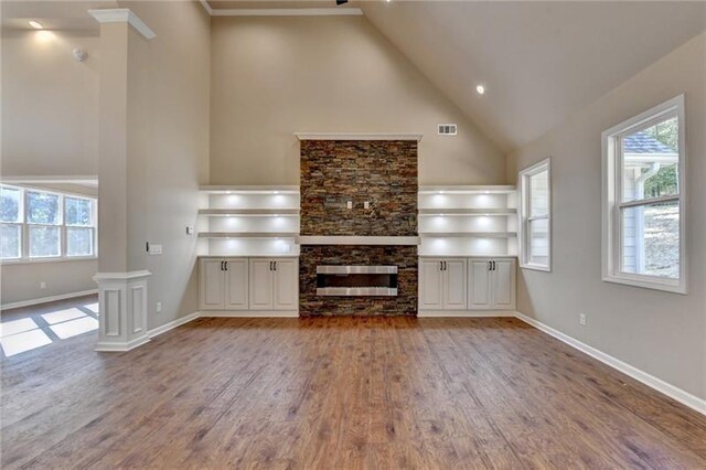unfurnished living room with high vaulted ceiling, a stone fireplace, baseboards, wood finished floors, and visible vents