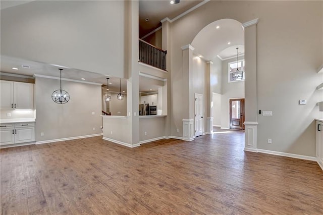 unfurnished living room with high vaulted ceiling, a chandelier, recessed lighting, baseboards, and wood finished floors