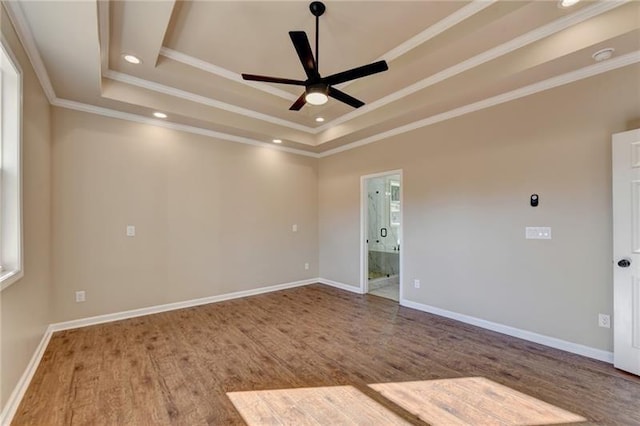 spare room with ceiling fan, baseboards, wood finished floors, a tray ceiling, and ornamental molding
