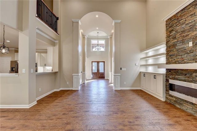 foyer featuring a fireplace, wood finished floors, baseboards, a chandelier, and a high ceiling