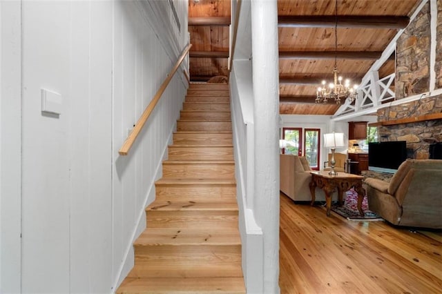 staircase with wood ceiling, vaulted ceiling with beams, wood-type flooring, a fireplace, and a chandelier