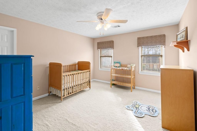 bedroom with ceiling fan, a nursery area, a textured ceiling, and carpet flooring