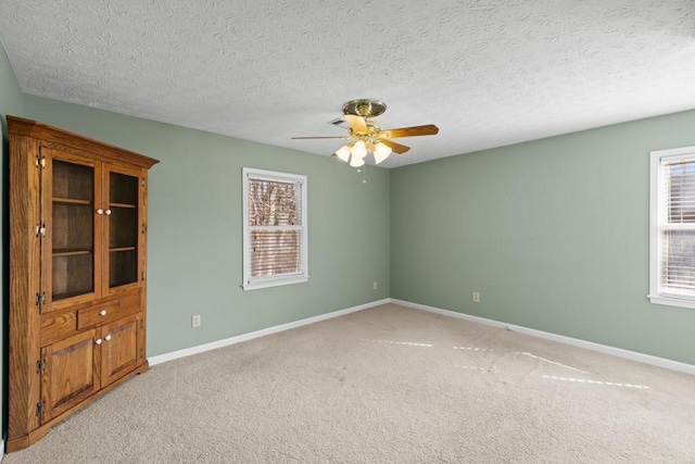 empty room featuring light carpet, a textured ceiling, plenty of natural light, and ceiling fan