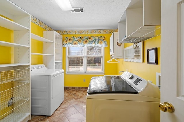 clothes washing area with washing machine and dryer, light tile patterned flooring, and a textured ceiling