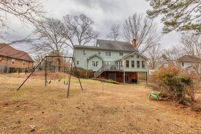 rear view of property with a playground, a wooden deck, and a lawn