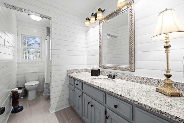 bathroom featuring vanity, wooden walls, toilet, and walk in shower