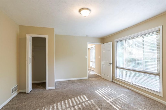 unfurnished bedroom featuring light colored carpet, a closet, multiple windows, and a walk in closet