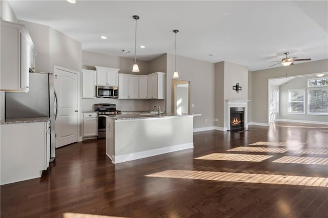 kitchen featuring white cabinetry, tasteful backsplash, hanging light fixtures, a center island with sink, and stainless steel appliances