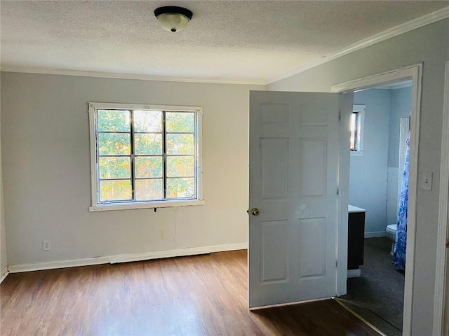 unfurnished bedroom with a textured ceiling, dark hardwood / wood-style floors, ornamental molding, and connected bathroom