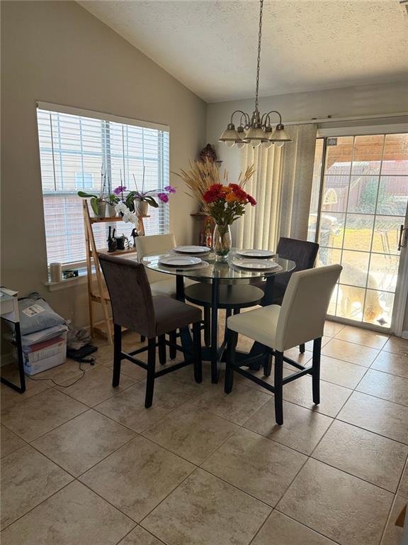 dining area featuring light tile patterned floors, a chandelier, vaulted ceiling, and a textured ceiling