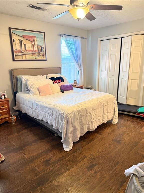 bedroom with visible vents, dark wood finished floors, a ceiling fan, a textured ceiling, and a closet