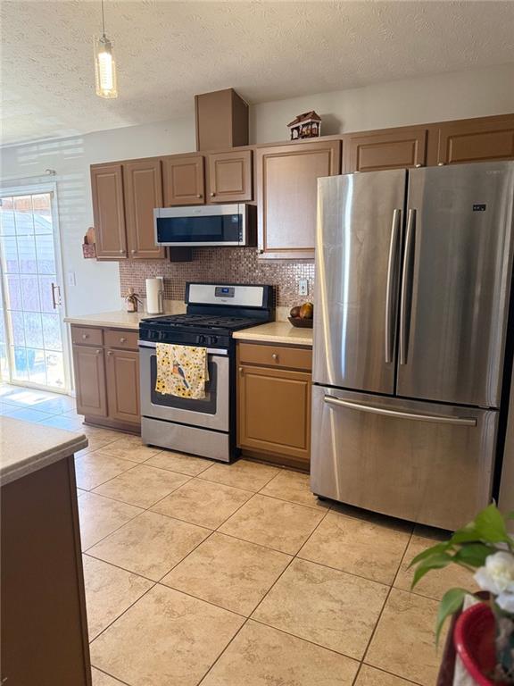 kitchen featuring decorative light fixtures, light tile patterned floors, stainless steel appliances, light countertops, and decorative backsplash