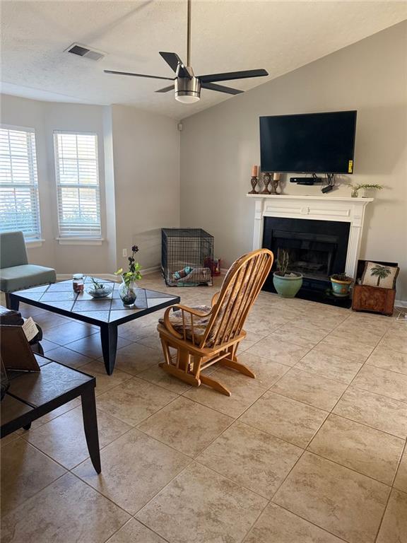 living area featuring light tile patterned floors, a fireplace, visible vents, and vaulted ceiling