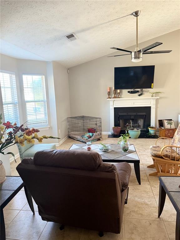 living room featuring baseboards, visible vents, a fireplace with raised hearth, vaulted ceiling, and a textured ceiling