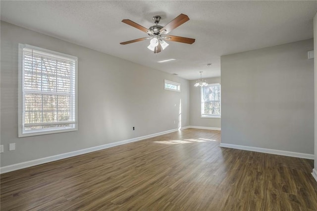 empty room with a textured ceiling, ceiling fan with notable chandelier, and dark wood-type flooring