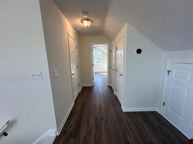 hall featuring a textured ceiling, dark hardwood / wood-style flooring, and vaulted ceiling