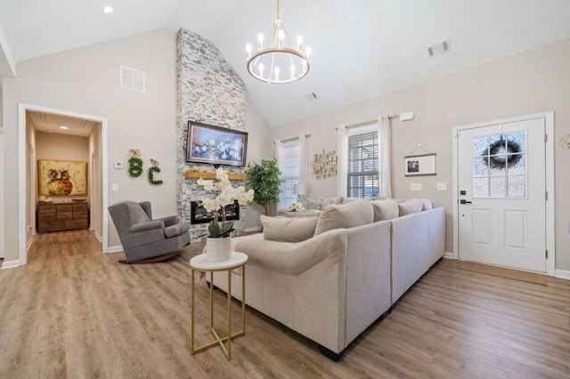 living room with wood-type flooring, an inviting chandelier, high vaulted ceiling, and a stone fireplace