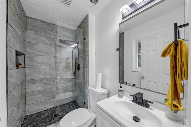 bathroom featuring vanity, a textured ceiling, toilet, and tiled shower