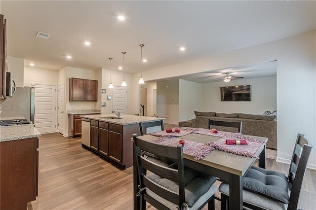 kitchen with sink, a kitchen island with sink, light stone counters, and hanging light fixtures