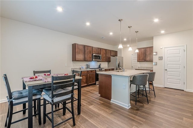 kitchen with stainless steel appliances, sink, light hardwood / wood-style flooring, hanging light fixtures, and a kitchen island with sink