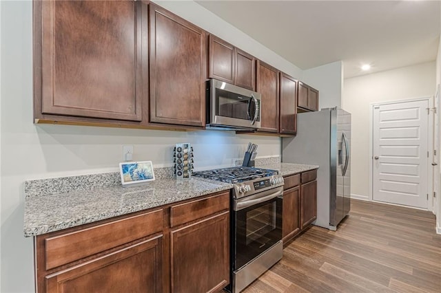 kitchen with light stone counters, stainless steel appliances, dark brown cabinetry, and hardwood / wood-style floors