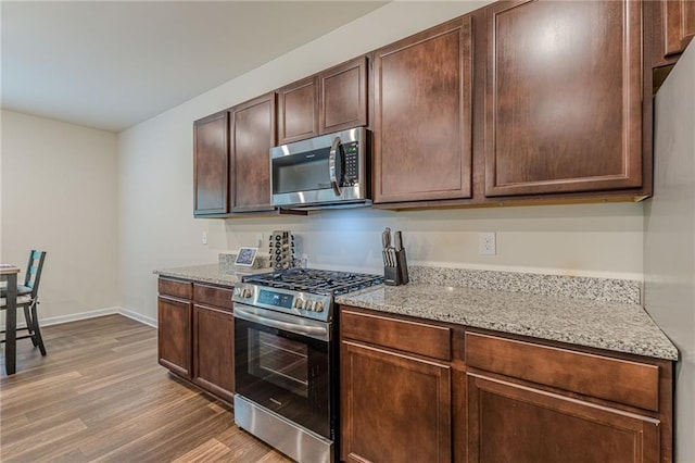 kitchen with light hardwood / wood-style floors, dark brown cabinets, light stone counters, and appliances with stainless steel finishes