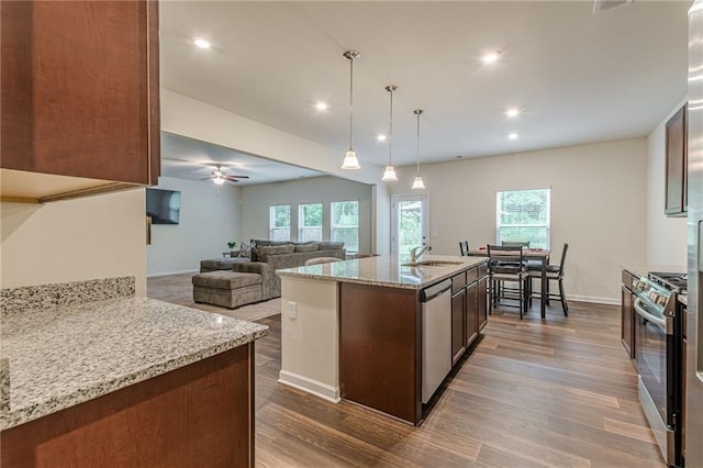 kitchen featuring light stone counters, pendant lighting, stainless steel appliances, a kitchen island with sink, and sink