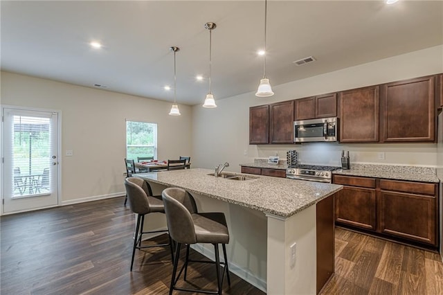 kitchen featuring stainless steel appliances, a center island with sink, light stone countertops, and hanging light fixtures