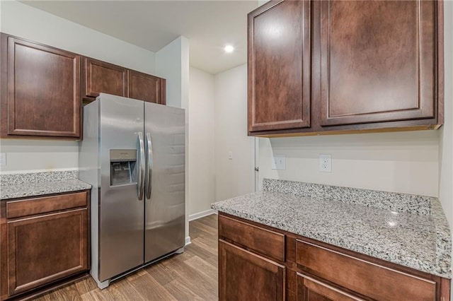 kitchen with light stone counters, light hardwood / wood-style floors, stainless steel fridge with ice dispenser, and dark brown cabinetry