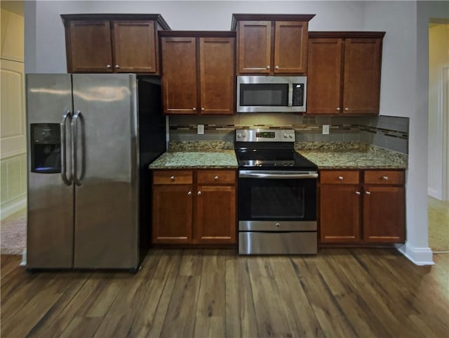 kitchen with dark hardwood / wood-style flooring, appliances with stainless steel finishes, light stone counters, and decorative backsplash