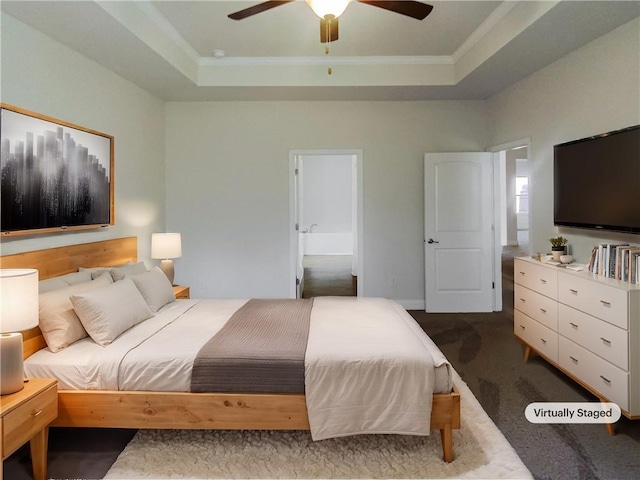 carpeted bedroom with ornamental molding, ensuite bath, ceiling fan, and a tray ceiling