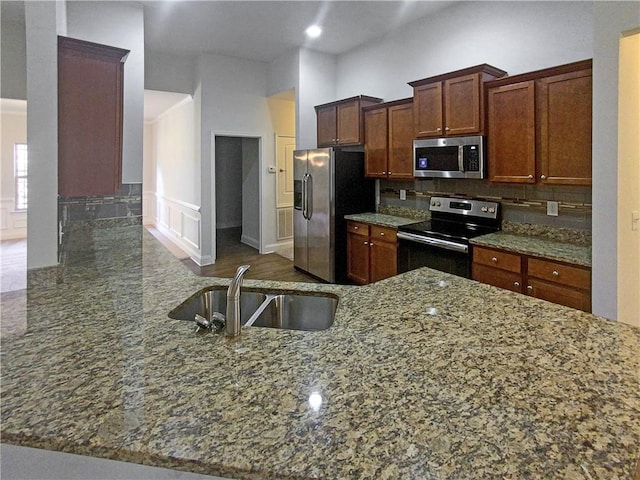 kitchen featuring sink, appliances with stainless steel finishes, kitchen peninsula, stone counters, and decorative backsplash