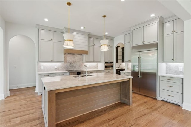 7188 Williams Rd, Flowery Branch, GA 30542 - kitchen with arched walkways, appliances with stainless steel finishes, a sink, decorative backsplash, and light wood-type flooring