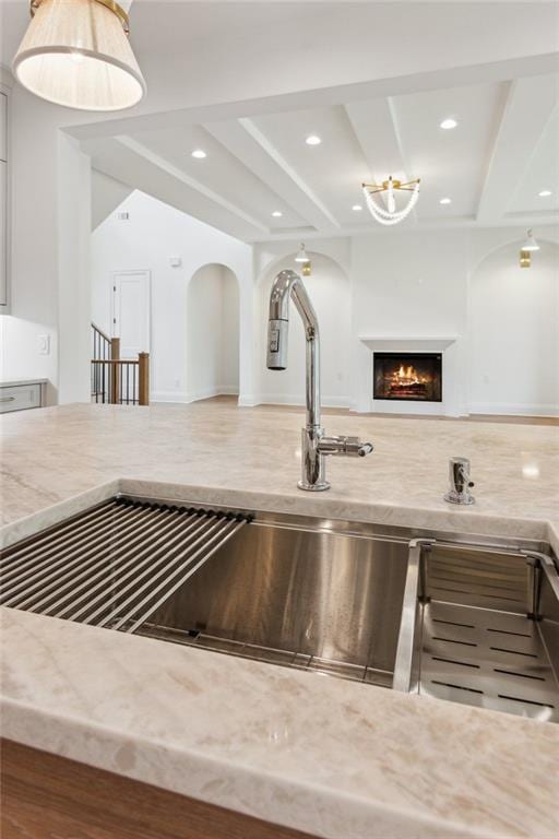 7188 Williams Rd, Flowery Branch, GA 30542 - kitchen view of light stone counters, a lit fireplace, recessed lighting, a sink, and arched walkways