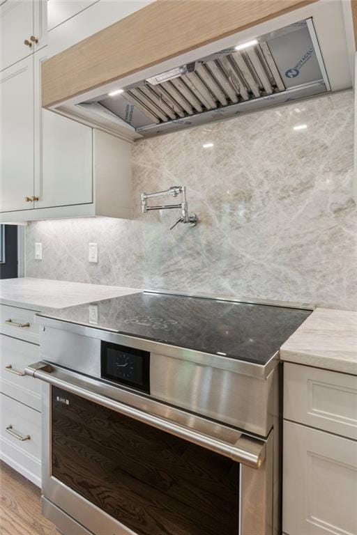 7188 Williams Rd, Flowery Branch, GA 30542 - kitchen with stainless steel electric range, premium range hood, white cabinetry, light stone countertops, and light wood-type flooring