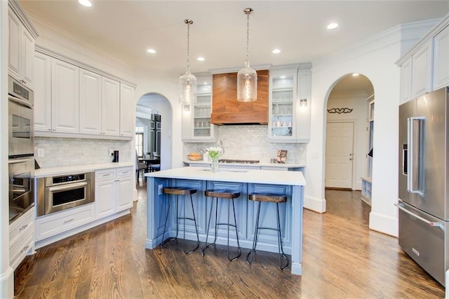 kitchen with light countertops, appliances with stainless steel finishes, glass insert cabinets, white cabinetry, and premium range hood