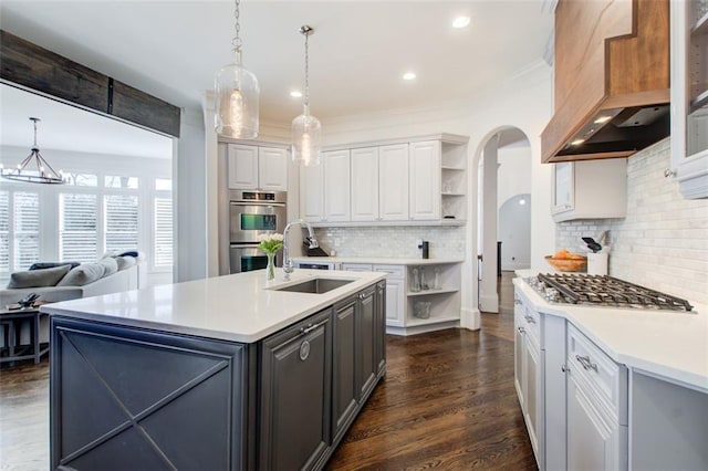 kitchen with custom exhaust hood, stainless steel appliances, light countertops, a kitchen island with sink, and a sink