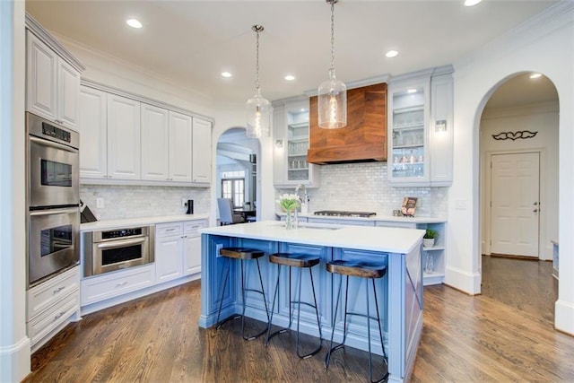 kitchen featuring glass insert cabinets, arched walkways, light countertops, and custom exhaust hood