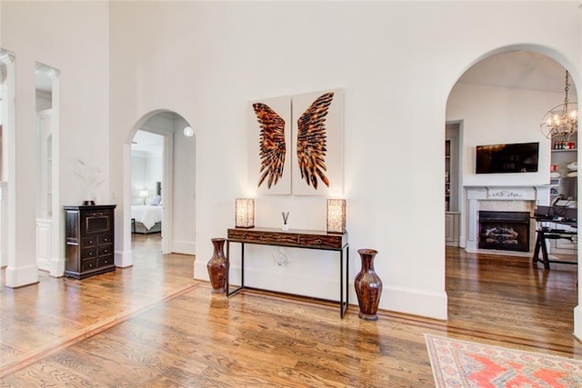 hall with a towering ceiling, baseboards, arched walkways, and wood finished floors